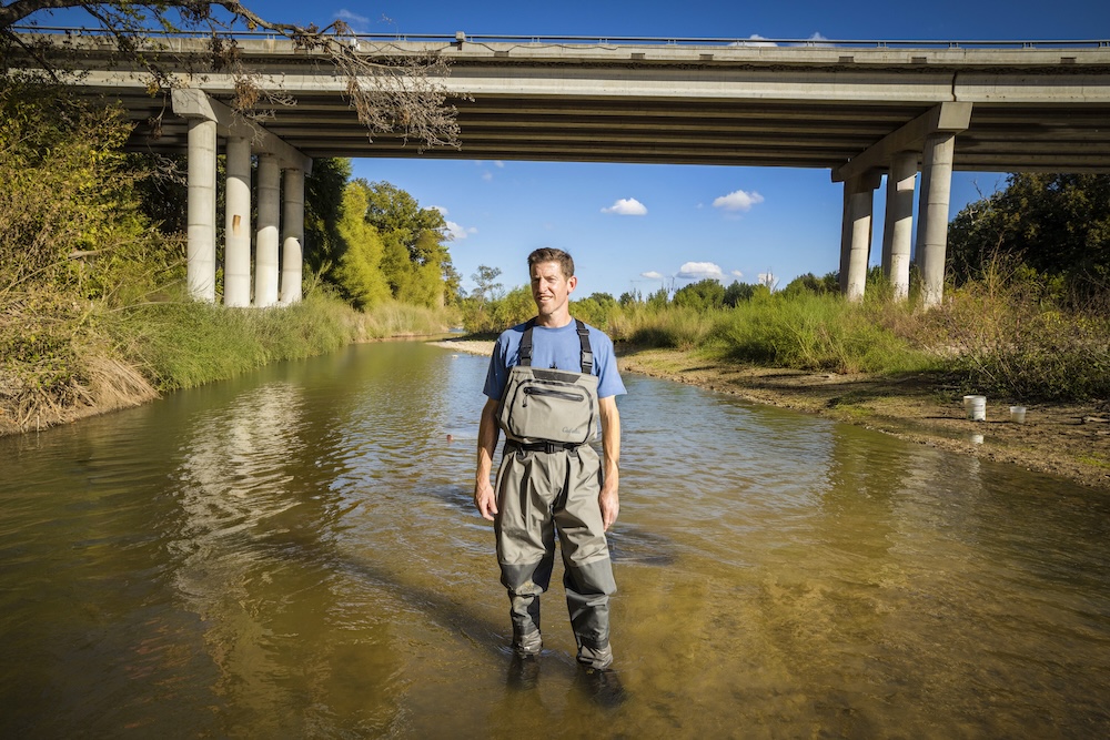 Ryan McManamay poses in a local stream under a highway bridge, highlighting intersection of environment and development